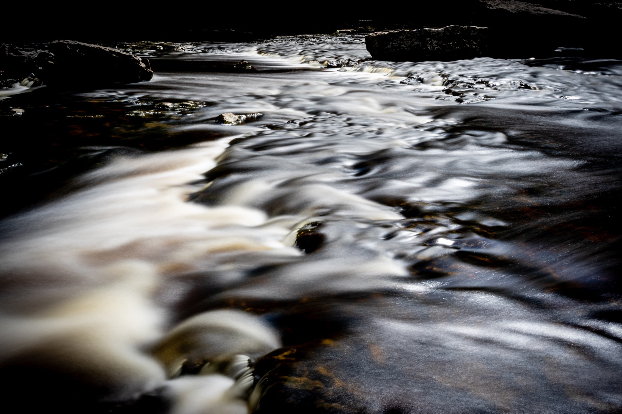 Long exposure of a serene stream with smooth water flowing over rocks, creating a silky effect.