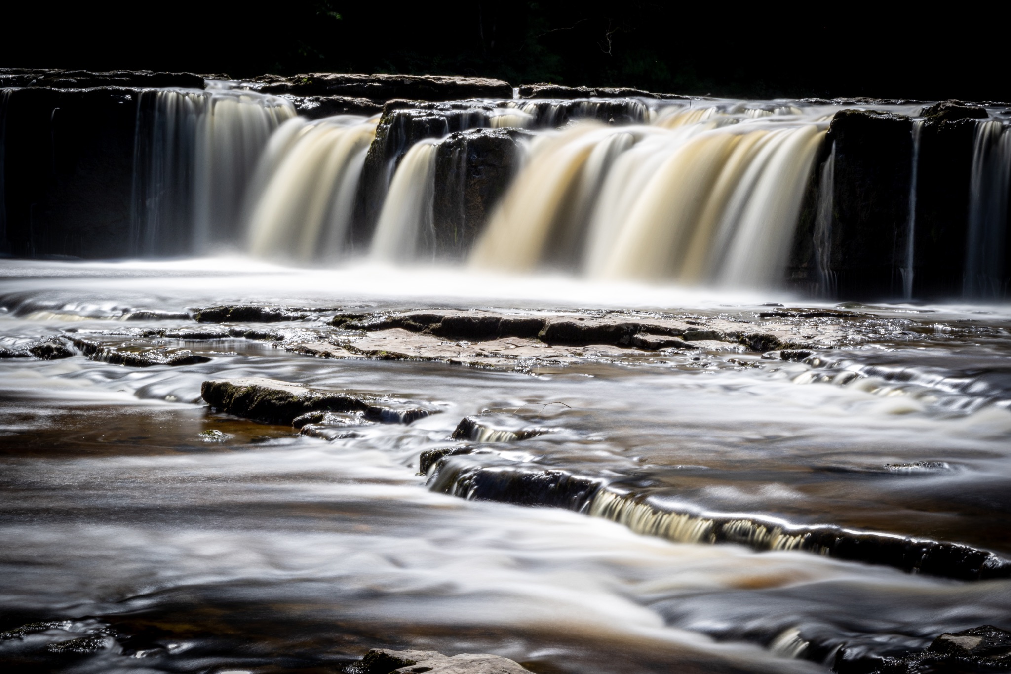 A serene waterfall with silky smooth water flowing over dark rocks, captured in a long exposure shot.