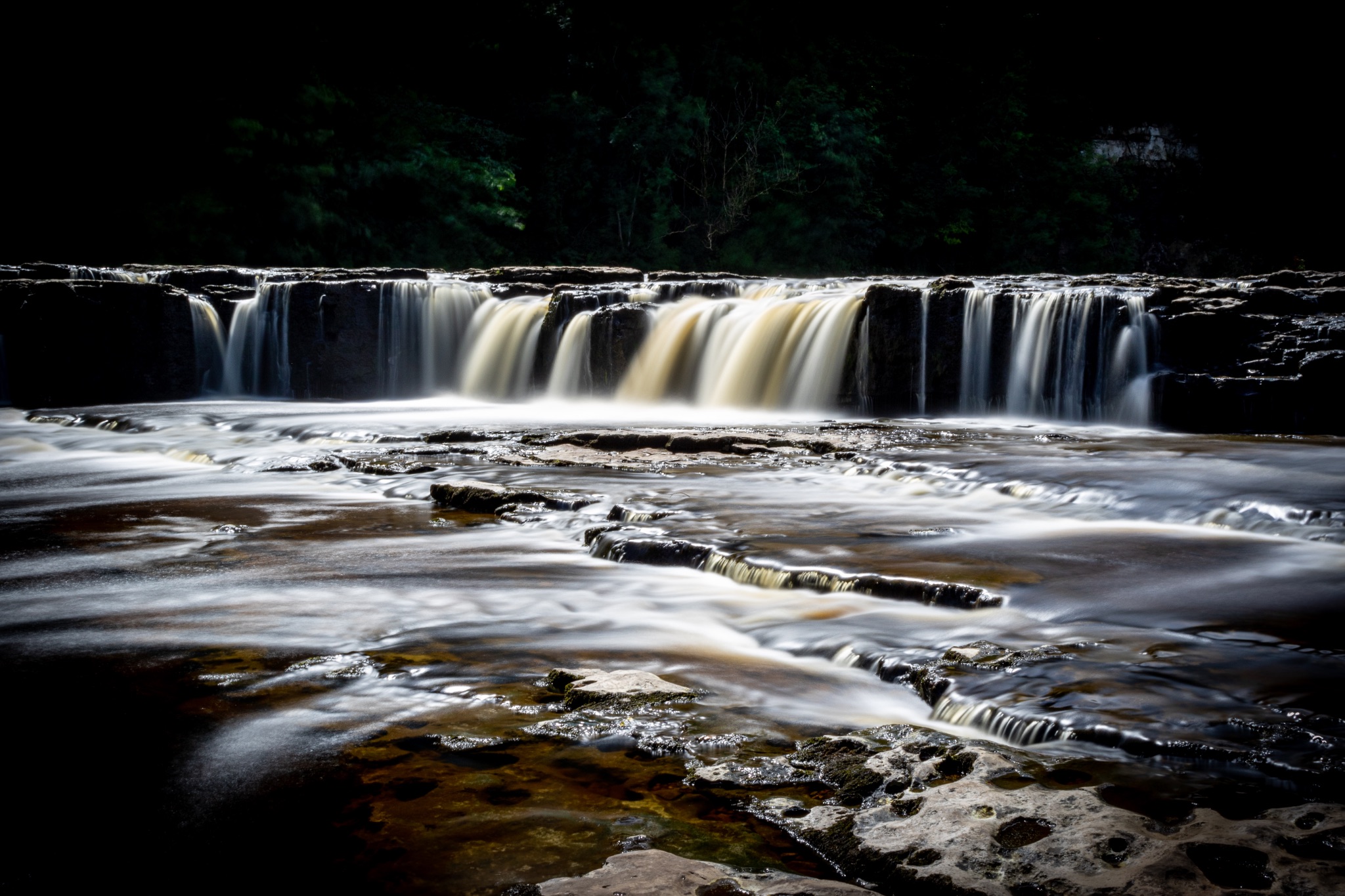 Silky smooth waterfall cascading over rocks with a dark, moody forest backdrop.