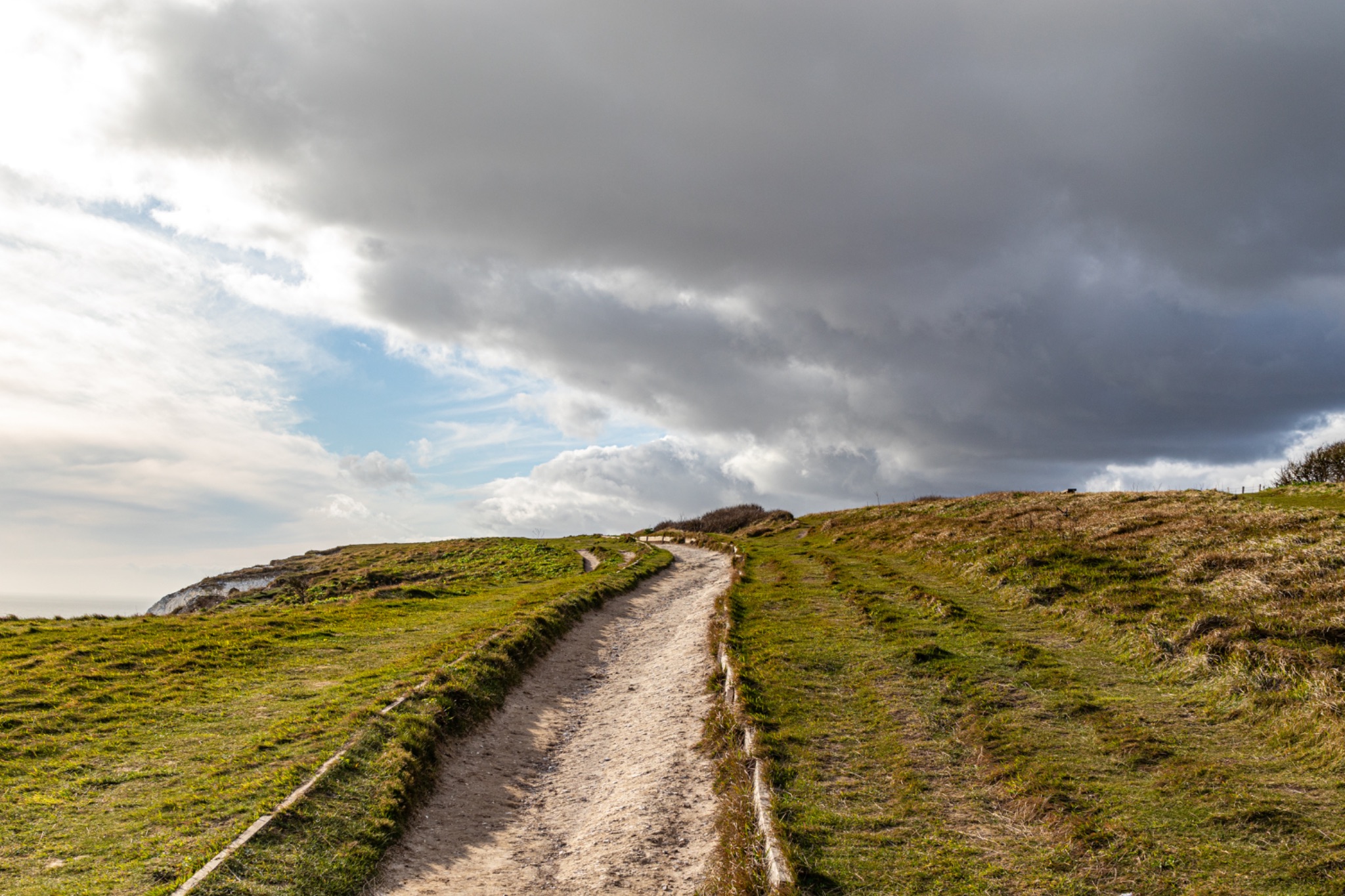 Dirt path through grassy hills under a dramatic cloudy sky