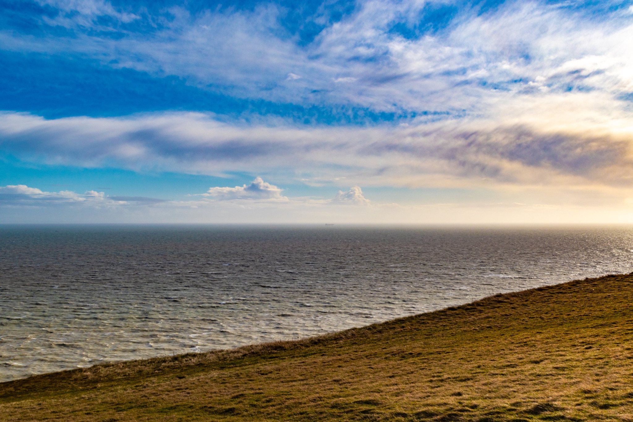 Serene coastal landscape with a vibrant blue sky, fluffy clouds, and calm sea, ideal for backgrounds and nature themes.