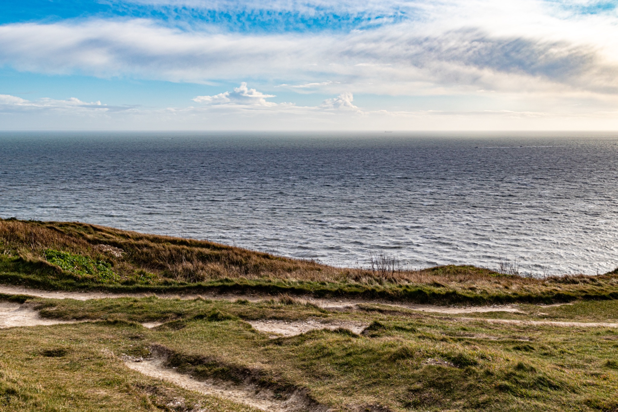 Coastal landscape with grassy cliffs and open sea under a blue sky with scattered clouds.