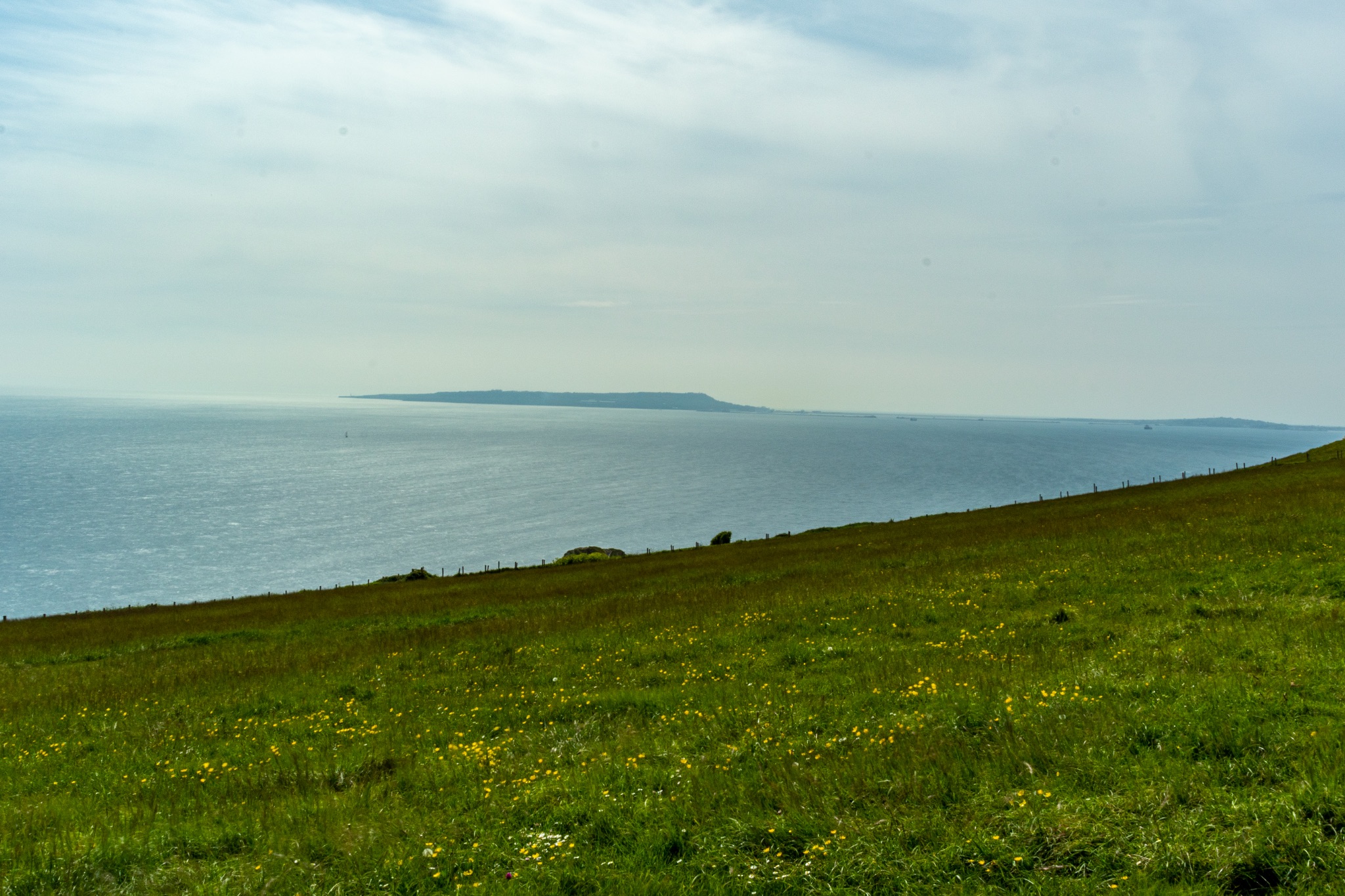 Tranquil coastal landscape with lush green grass and calm blue sea under a hazy sky at Durdle Door, England.