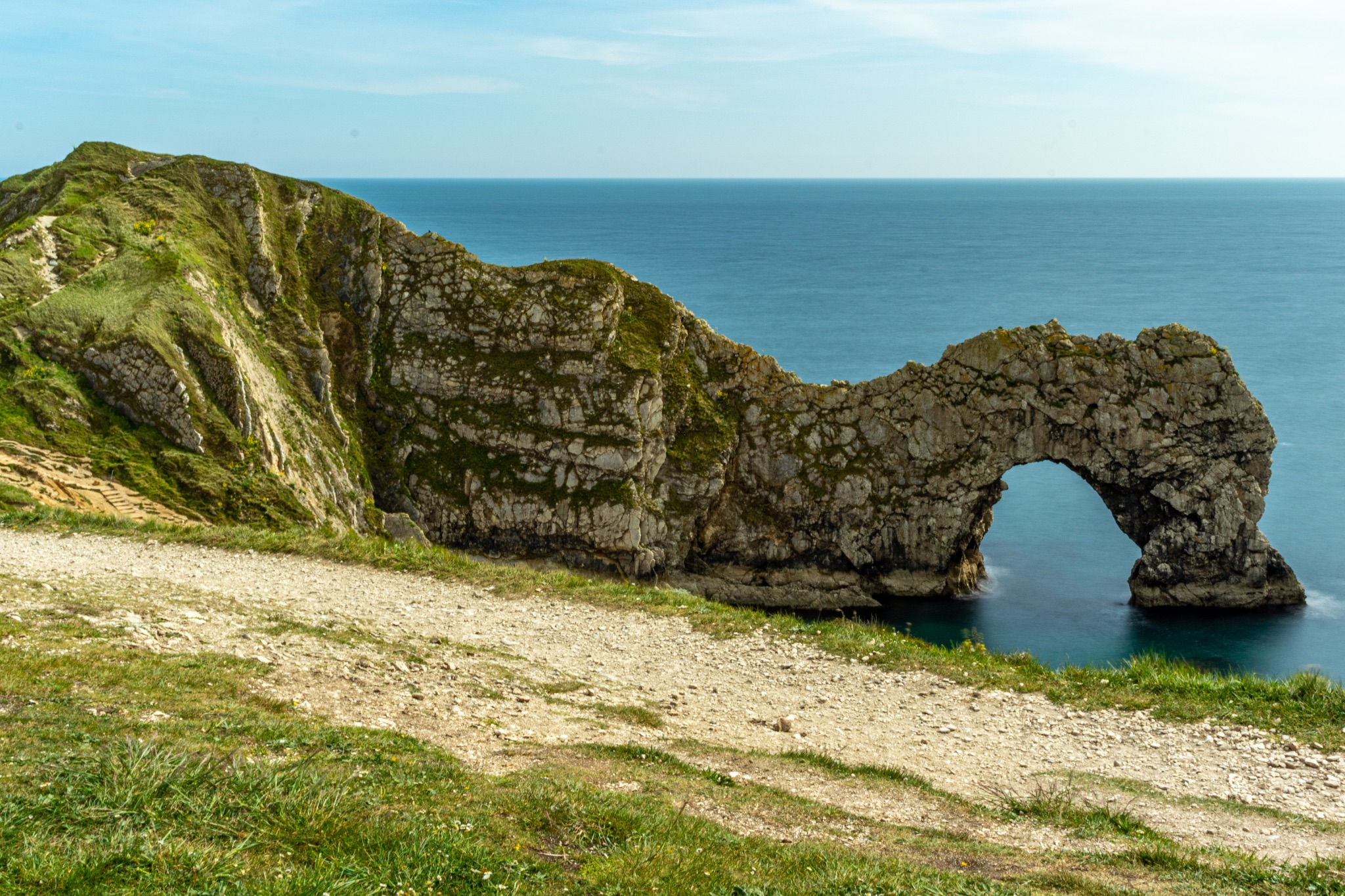 Scenic view of a natural rock arch on a coastline with a clear blue sky at Durdle Door, England.