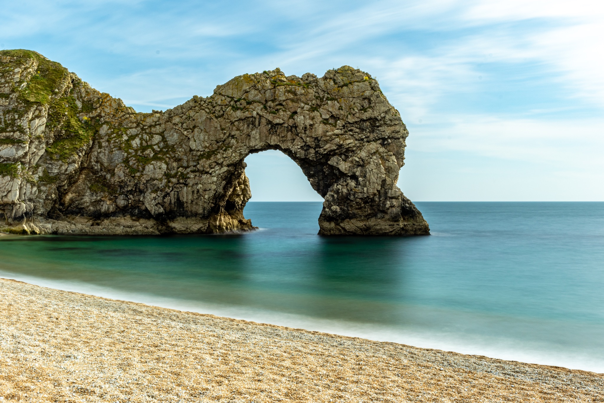 Natural rock arch on a serene beach with calm blue waters under a clear sky at Durdle Door, England.