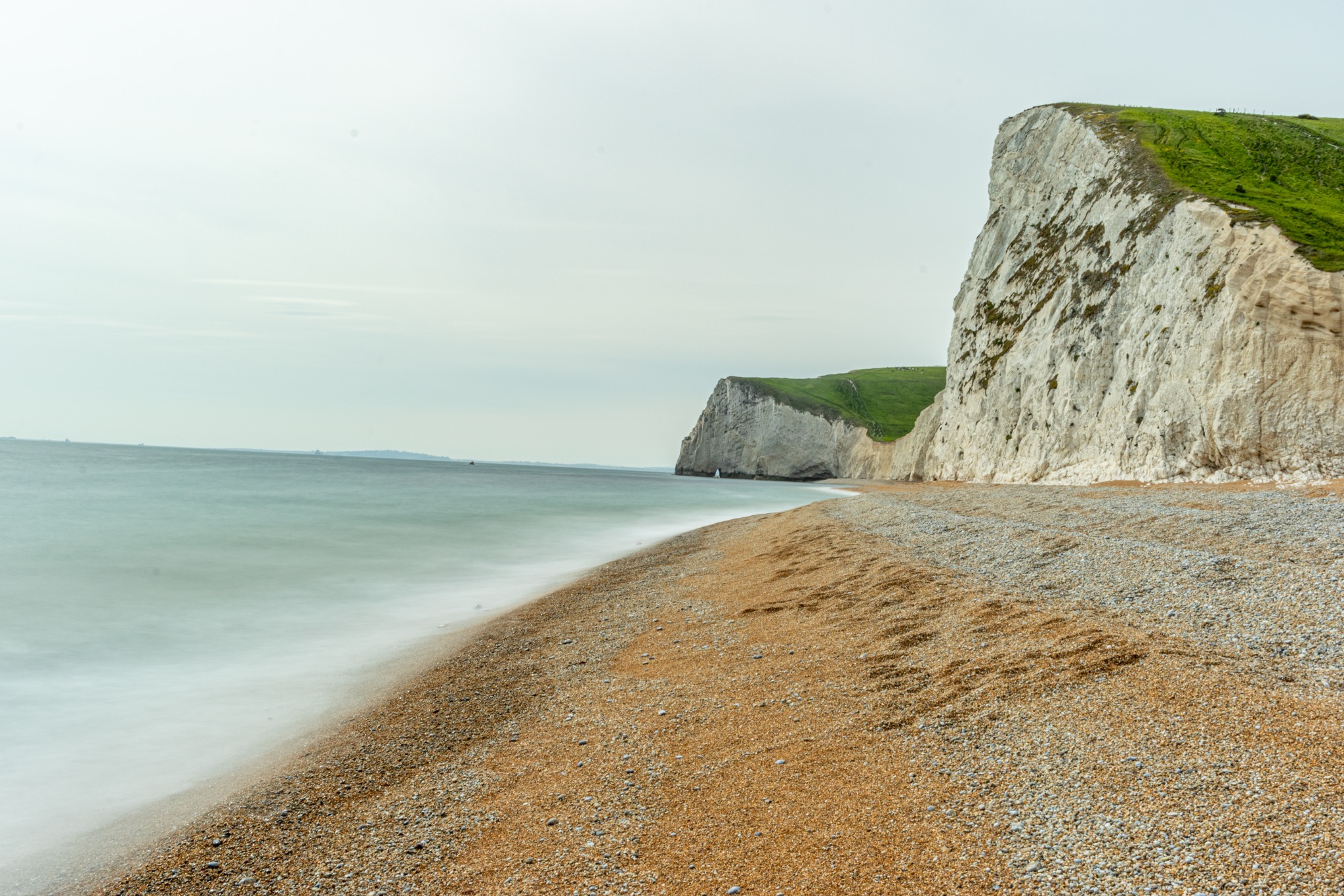 Serene beach with chalk cliffs and smooth sea under overcast sky at Durdle Door, England.