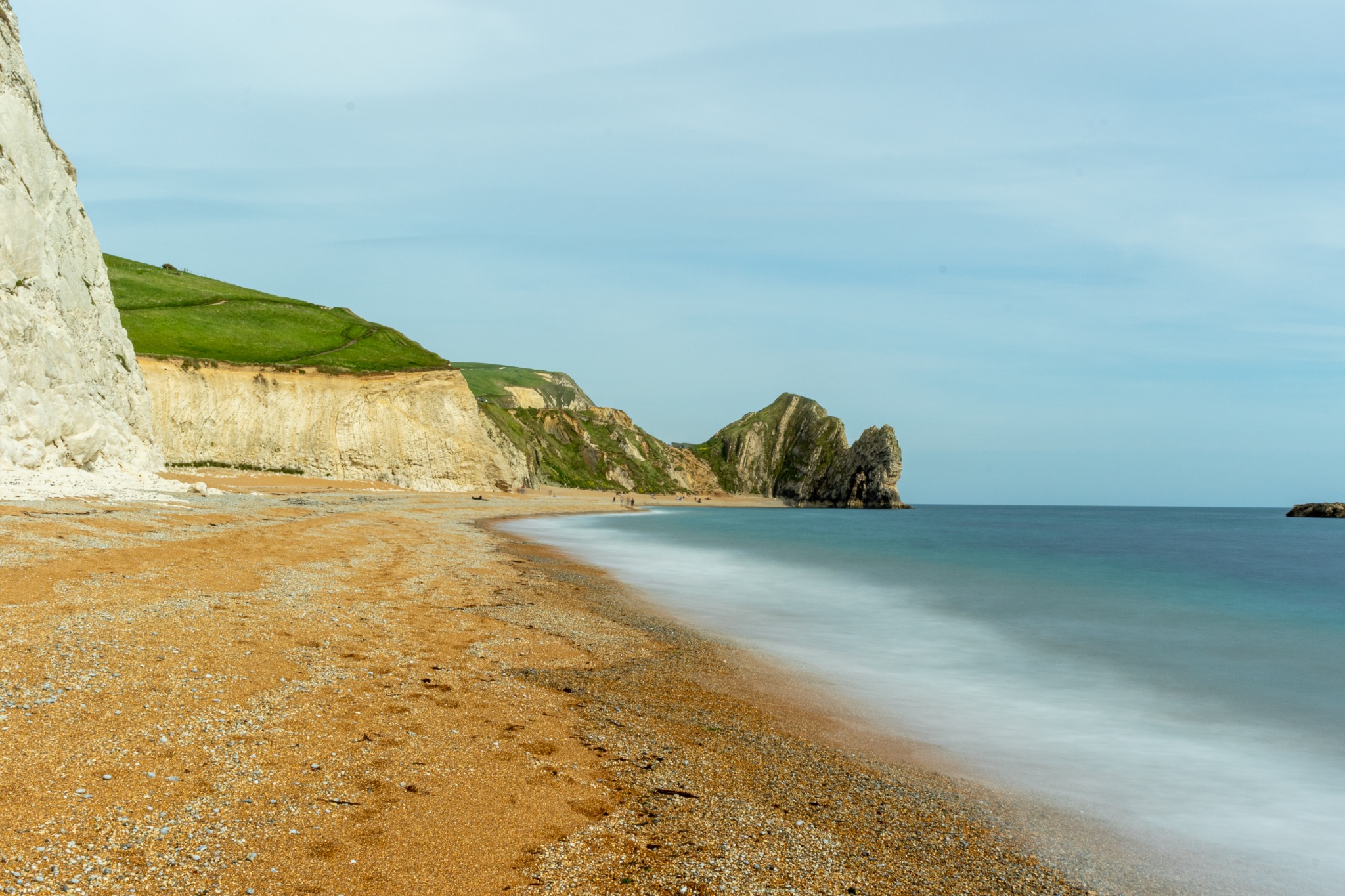 Serene beach with smooth water, sandy shore, and rugged cliffs under a clear sky at Durdle Door, England.
