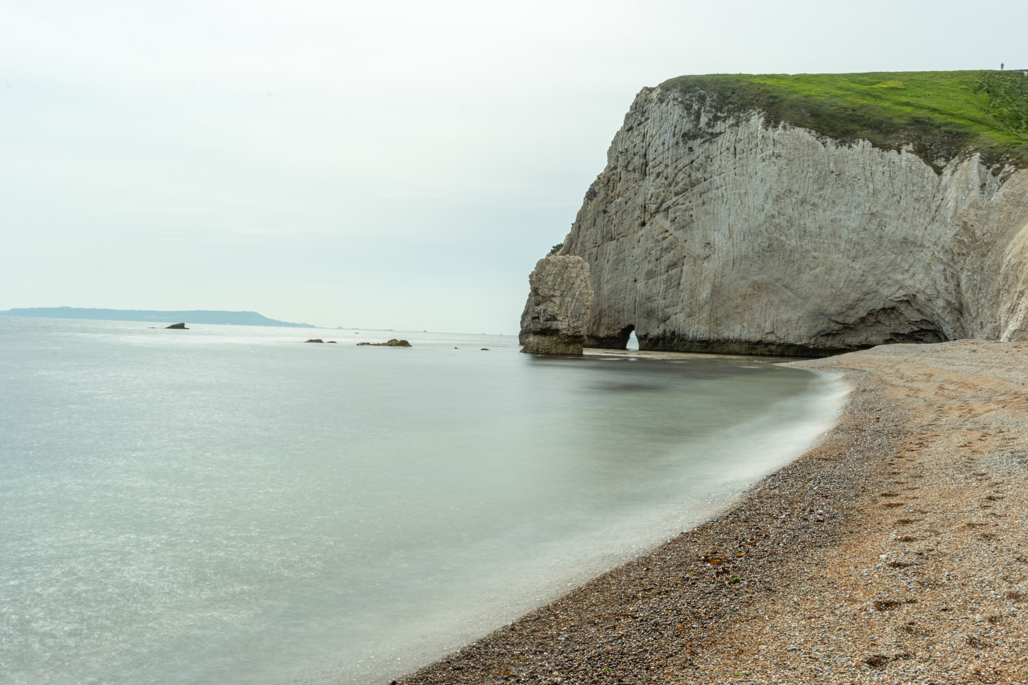 Serene beach with a cliff and calm sea, overcast sky, tranquil nature scene at Durdle Door, England.