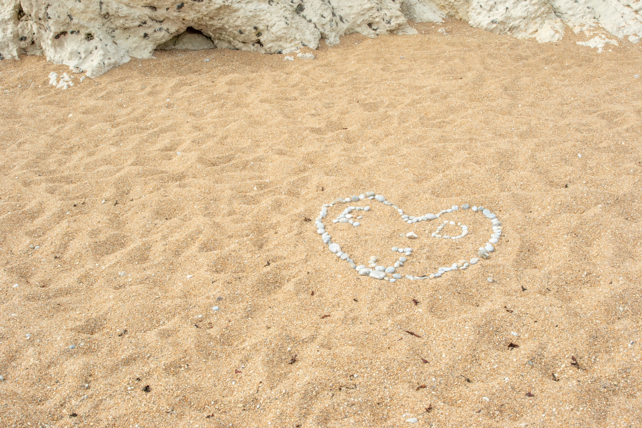 Heart shape made of seashells on sandy beach with rocks in background at Durdle Door, England.