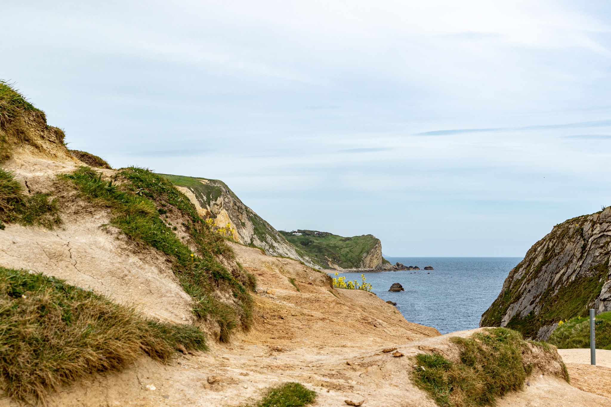 Coastal landscape with sandy cliffs and green vegetation under a cloudy sky, with a view of the ocean horizon at Durdle Door, England.
