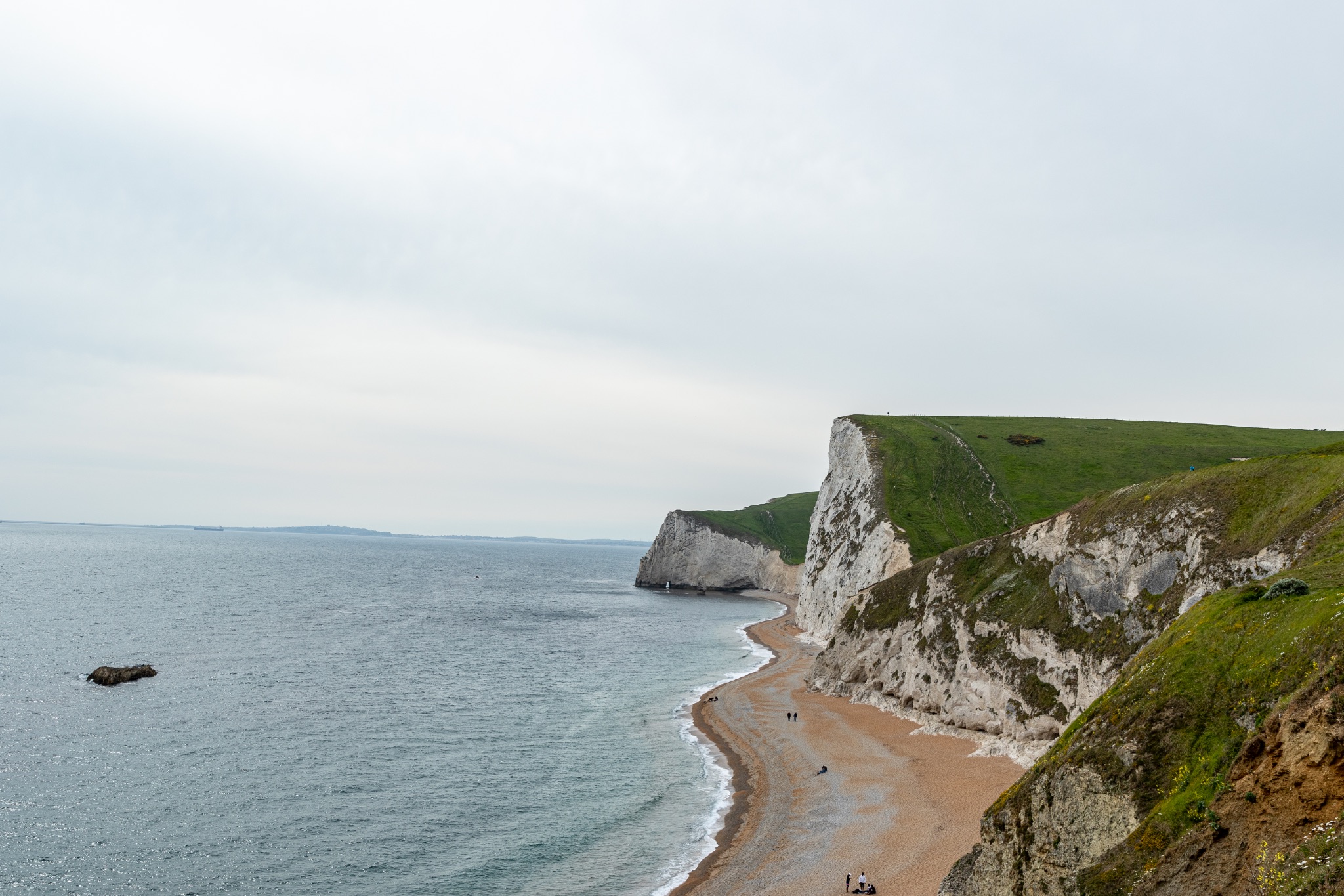 Serene coastal landscape with chalk cliffs and a sandy beach under a cloudy sky at Durdle Door, England.