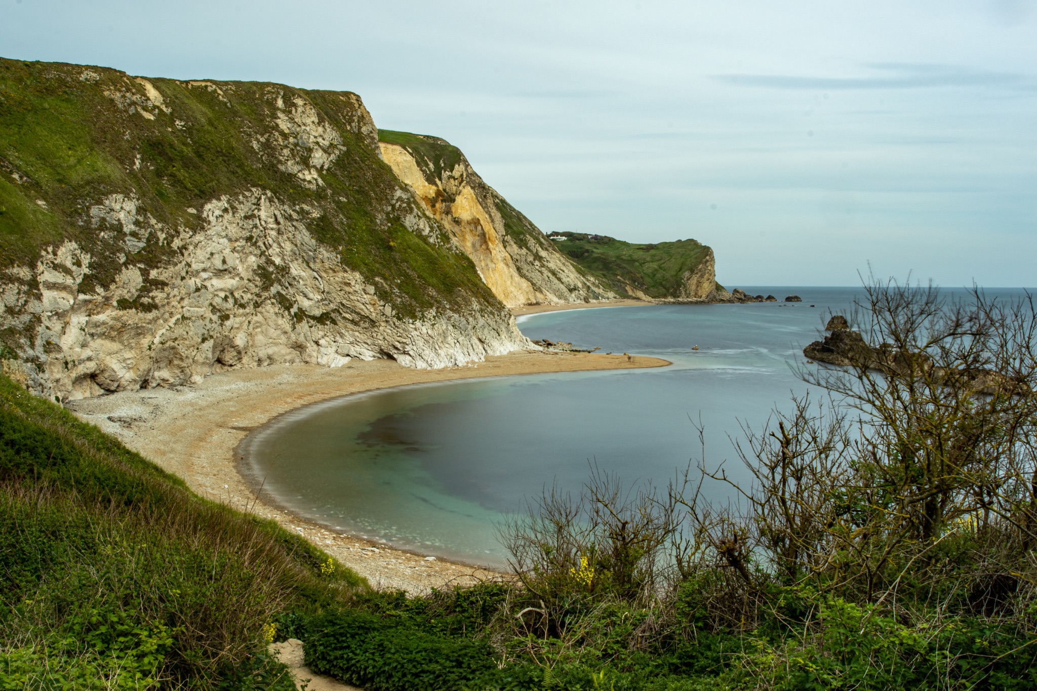 Scenic view of a tranquil cove with a sandy beach, surrounded by rugged cliffs under a clear blue sky at Durdle Door, England.