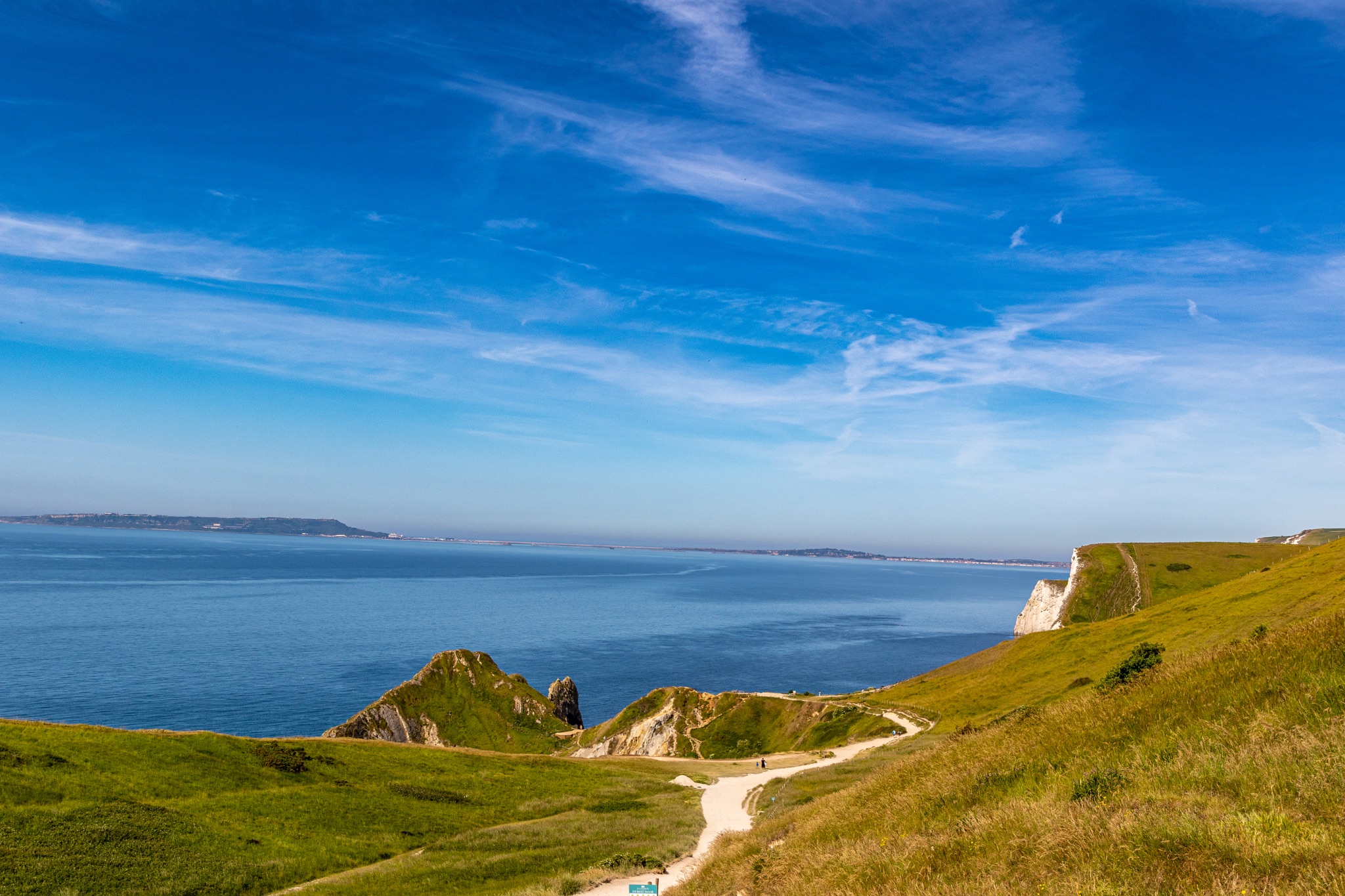 Scenic coastal landscape with green cliffs and a clear blue sky at Durdle Door, England.