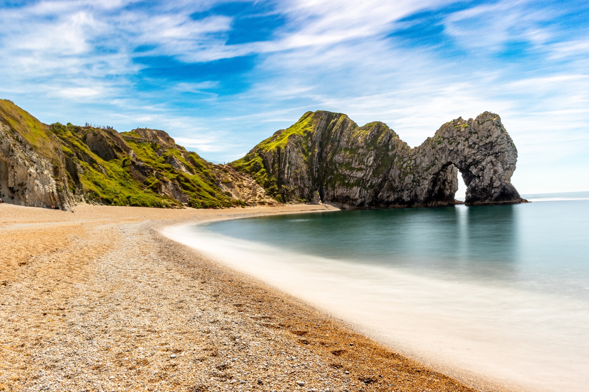 Sunny beach with a natural rock arch and clear blue sky at Durdle Door, England.