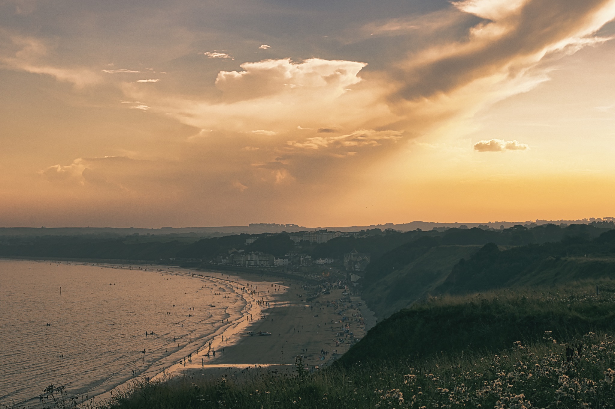 Scenic coastal sunset with golden sky, overlooking a tranquil sea and distant cliffs in Filey, England.