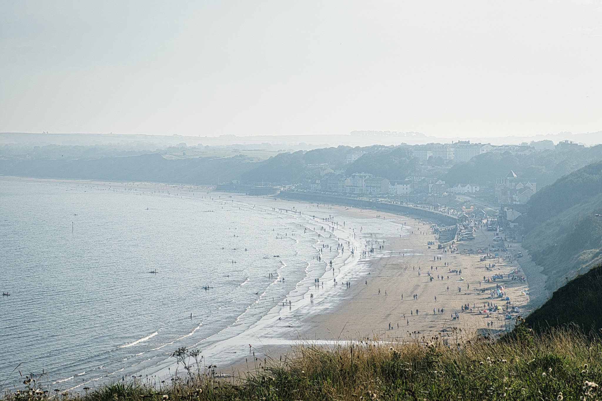 Misty coastal landscape with beach and hills, soft light, tranquil seaside town view in Filey, England.