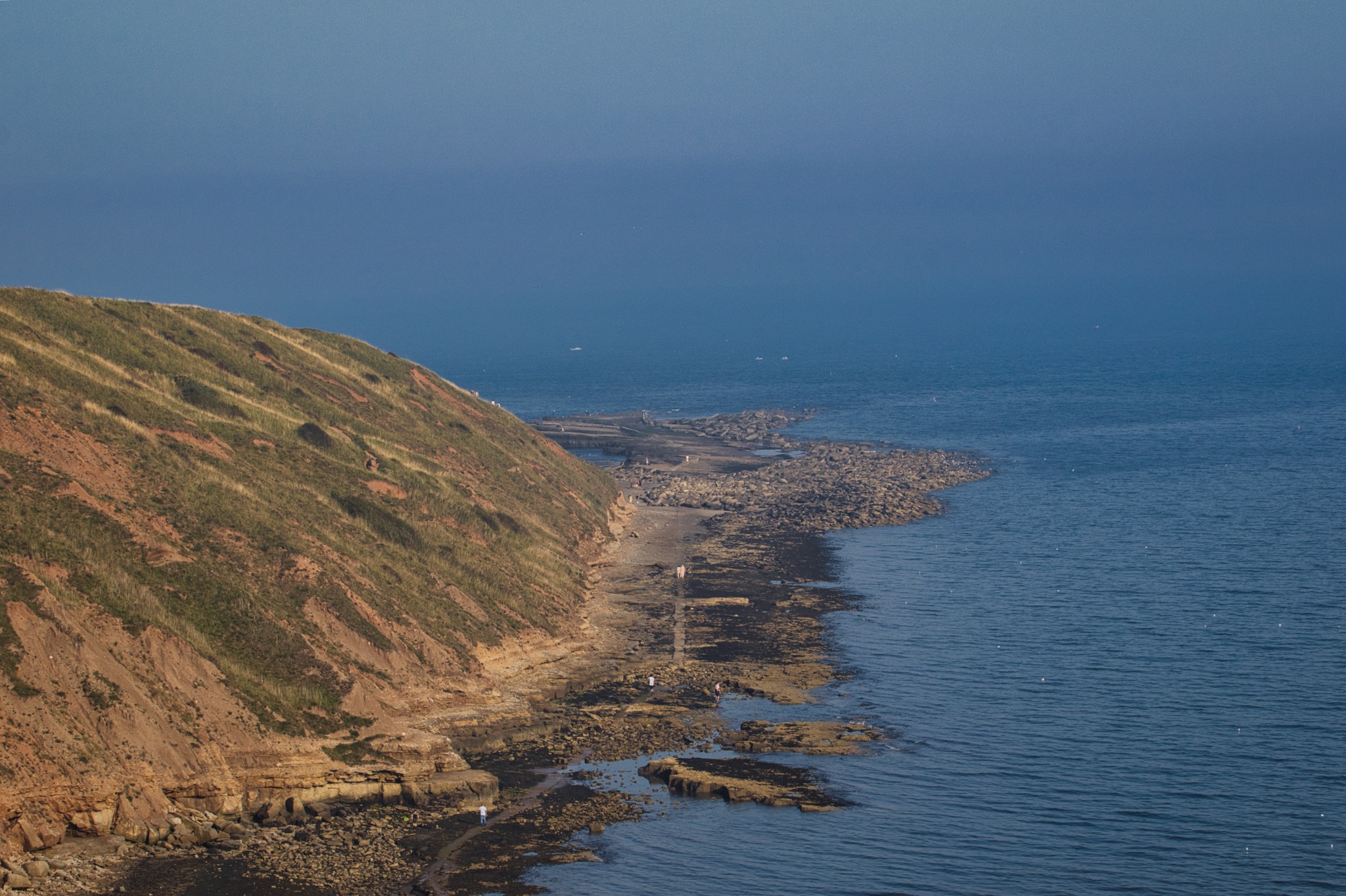 Coastal landscape with a serene blue ocean beside a rugged cliff under a clear sky in Filey, England.