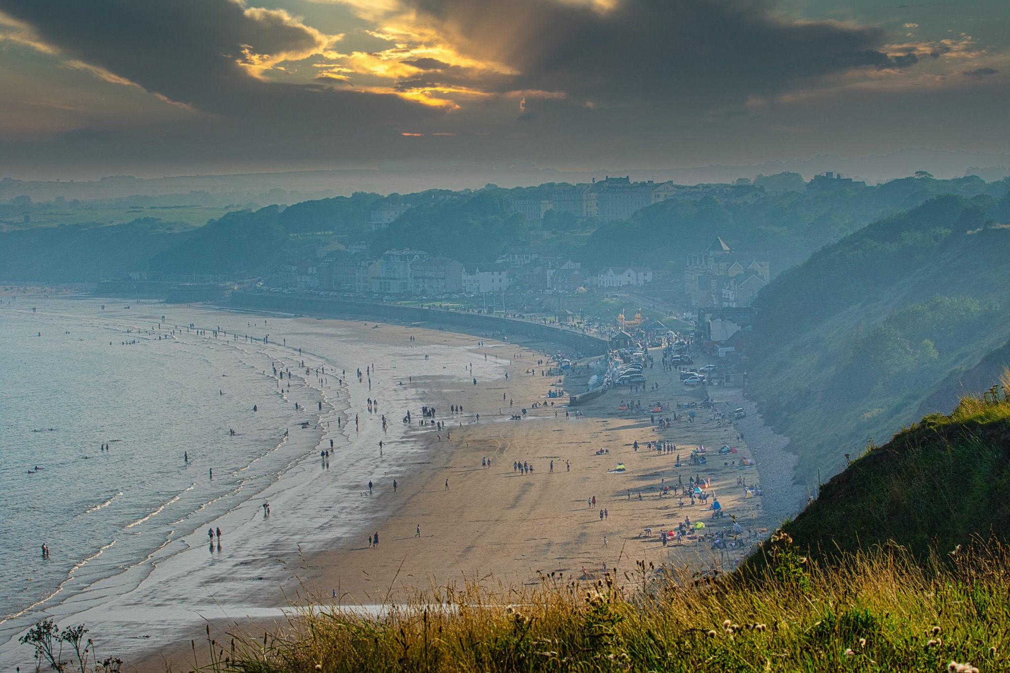 Scenic view of a sunlit beach with mountains in the background and dramatic clouds in the sky in Filey, England.