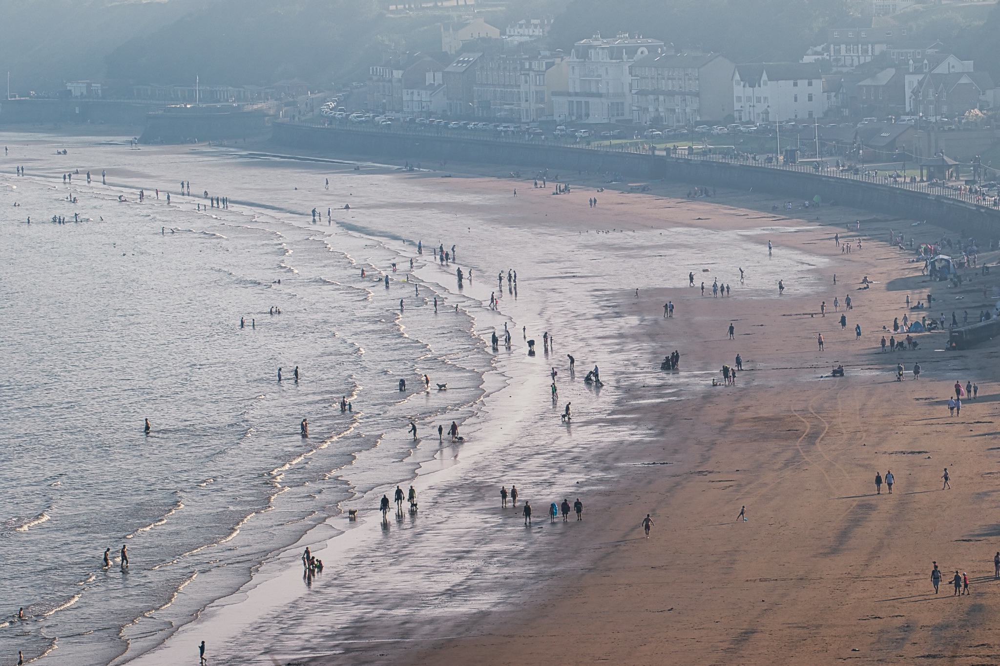 Aerial view of a crowded beach with waves and people walking on the sand in Filey, England.