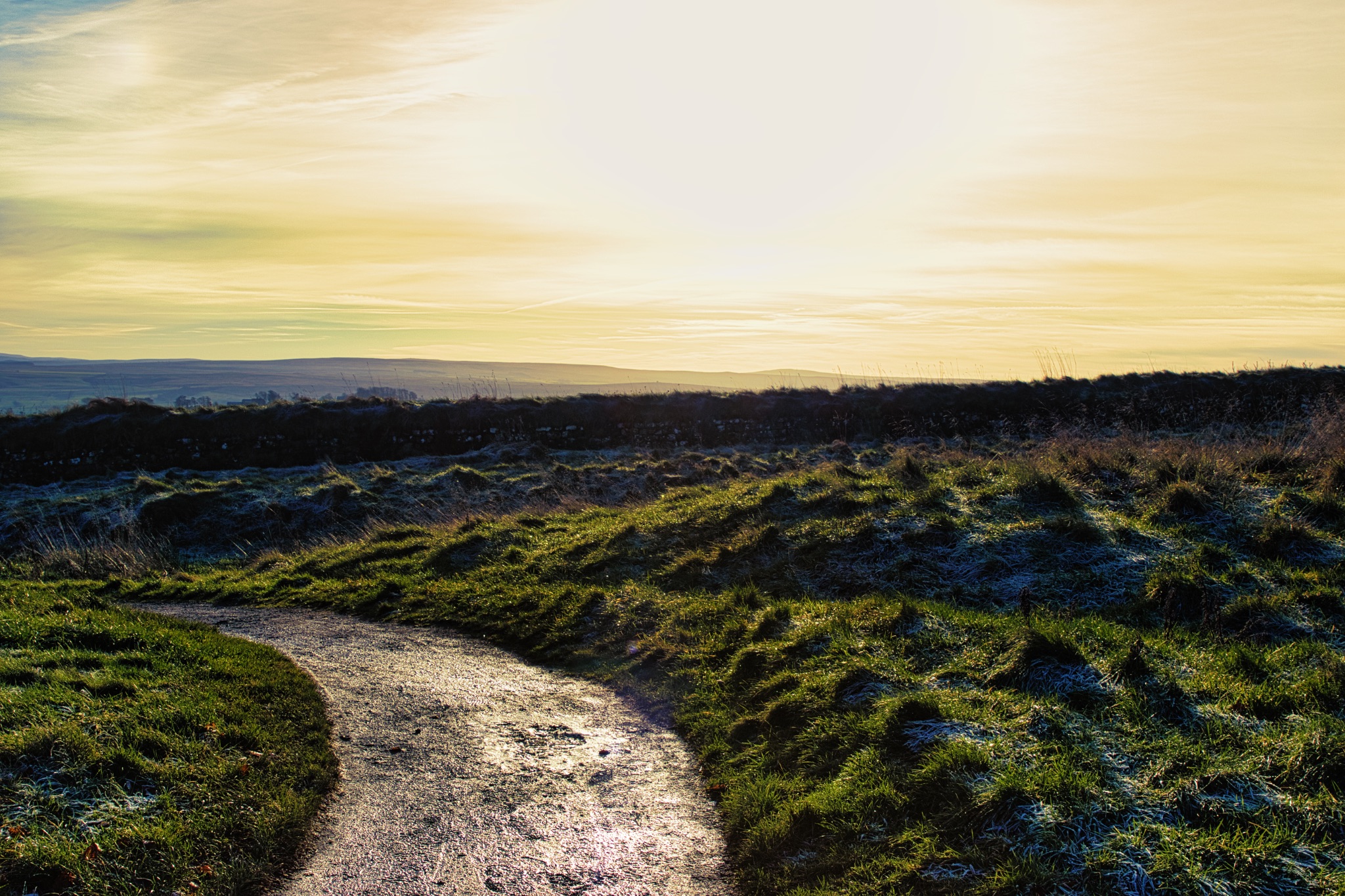 Sunny landscape with a winding path through grassy hills during golden hour, conveying a sense of tranquility and adventure.