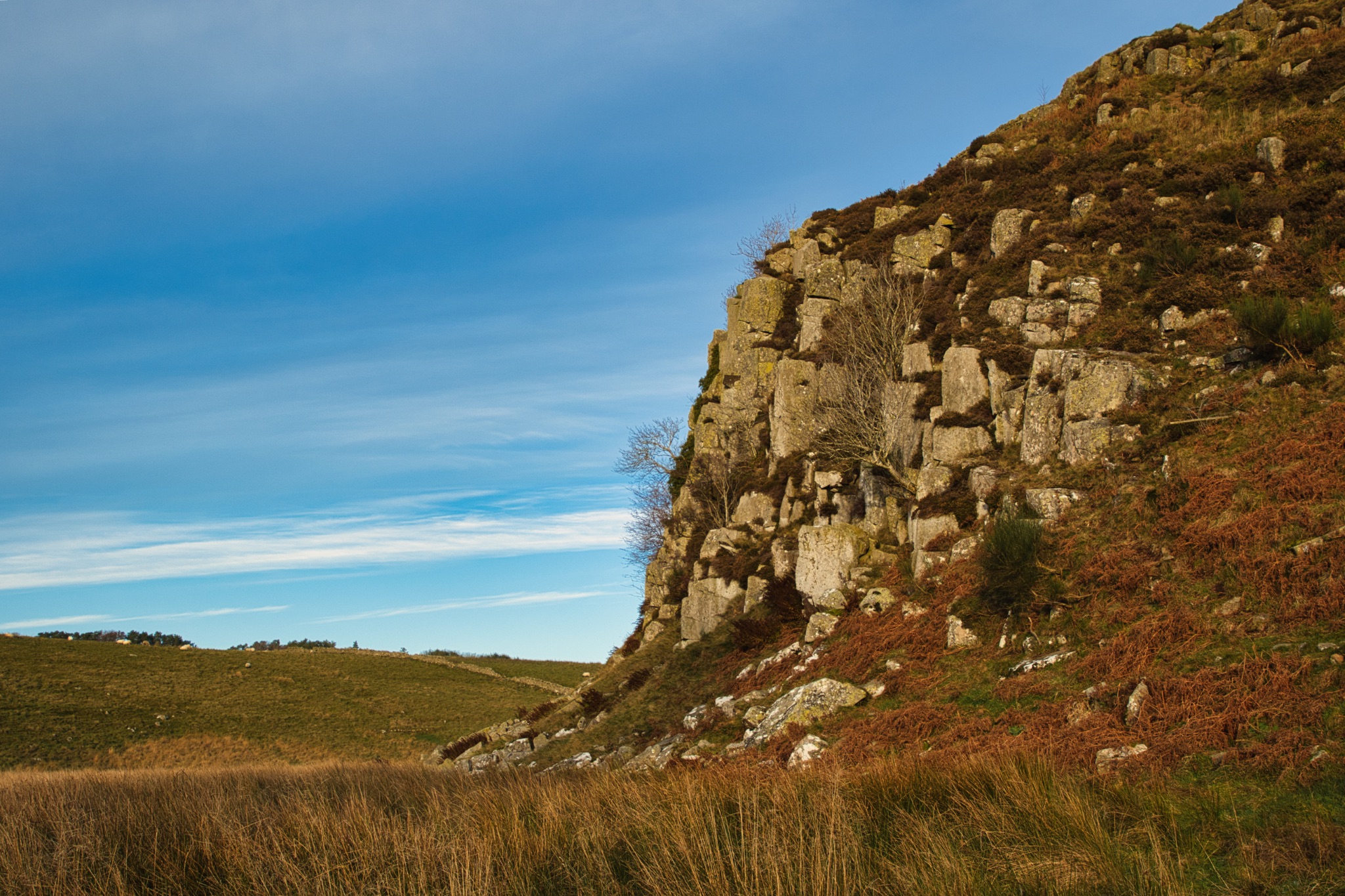 Rocky hillside with grass and blue sky at Sycamore Gap, Northumberland, UK.