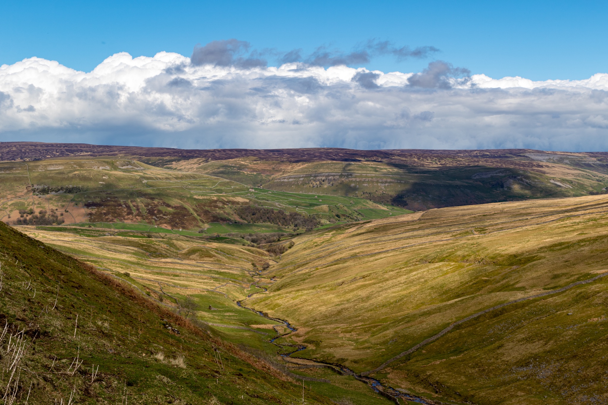 Rolling hills with green valleys under a cloudy blue sky, showcasing natural beauty and serene landscapes.