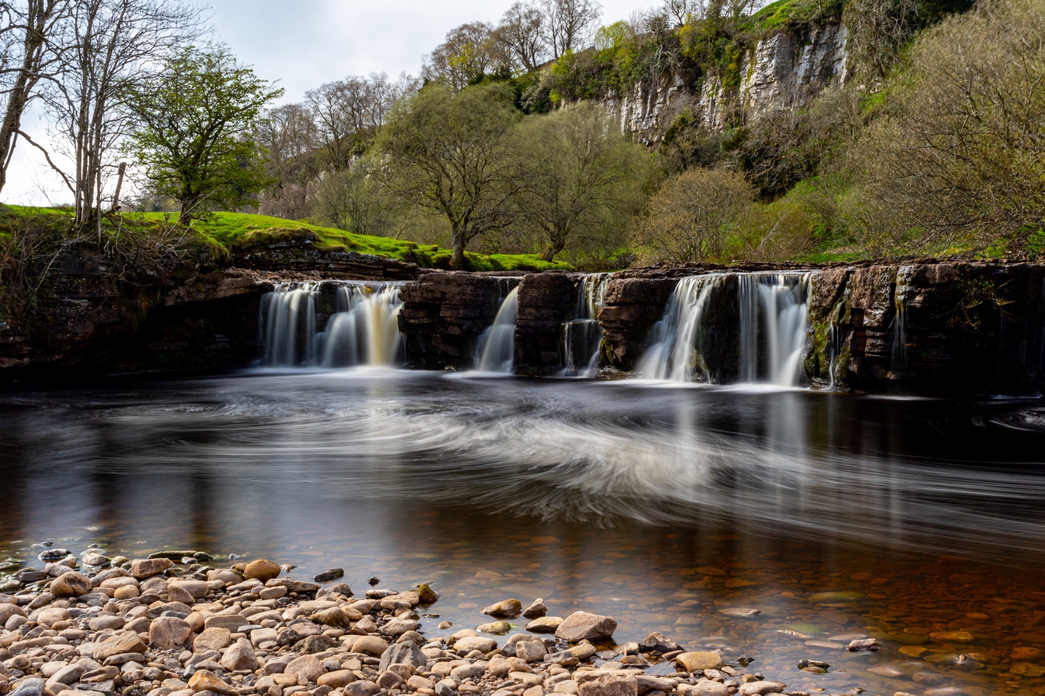 Tranquil waterfall with smooth flowing water in a lush green landscape, serene nature scene.