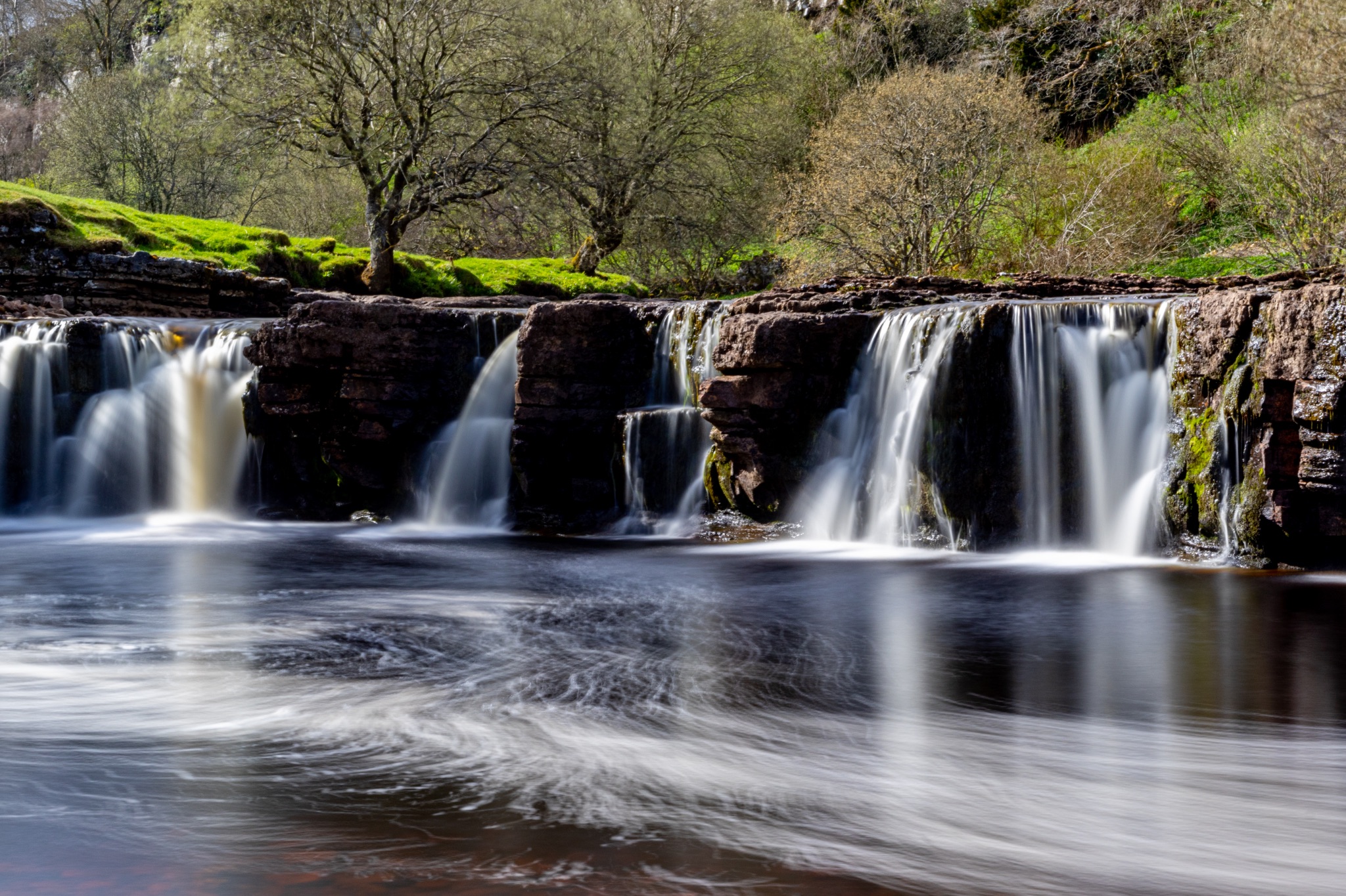 Serene waterfall with smooth water flow in a lush green landscape.