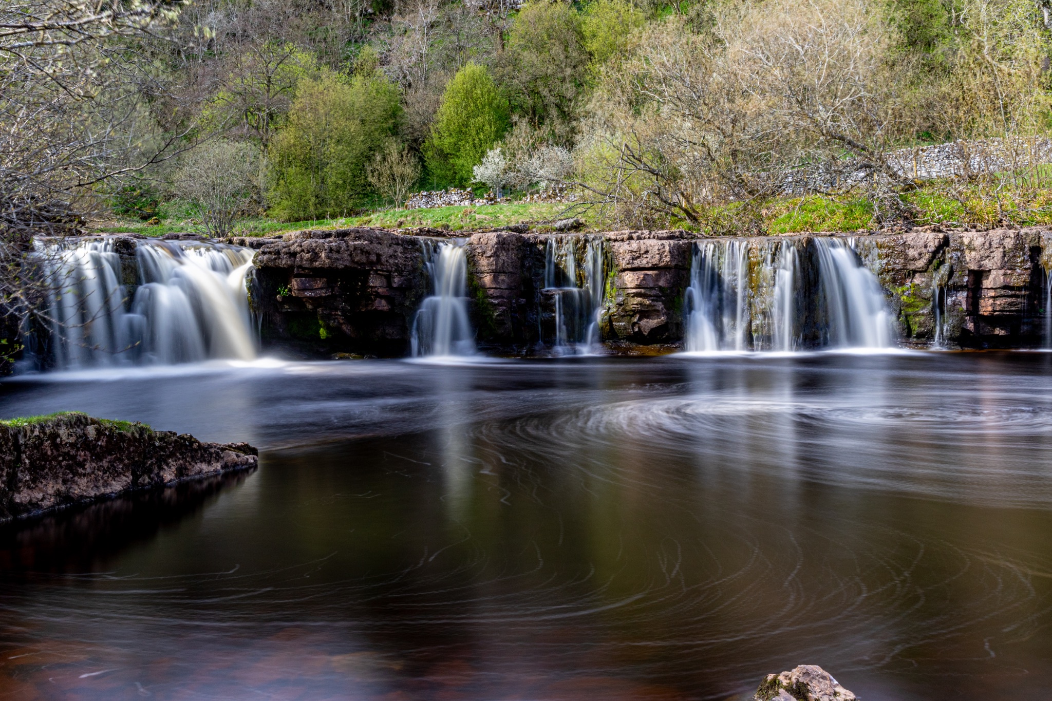 Serene waterfall with smooth flowing water and lush greenery in the background.