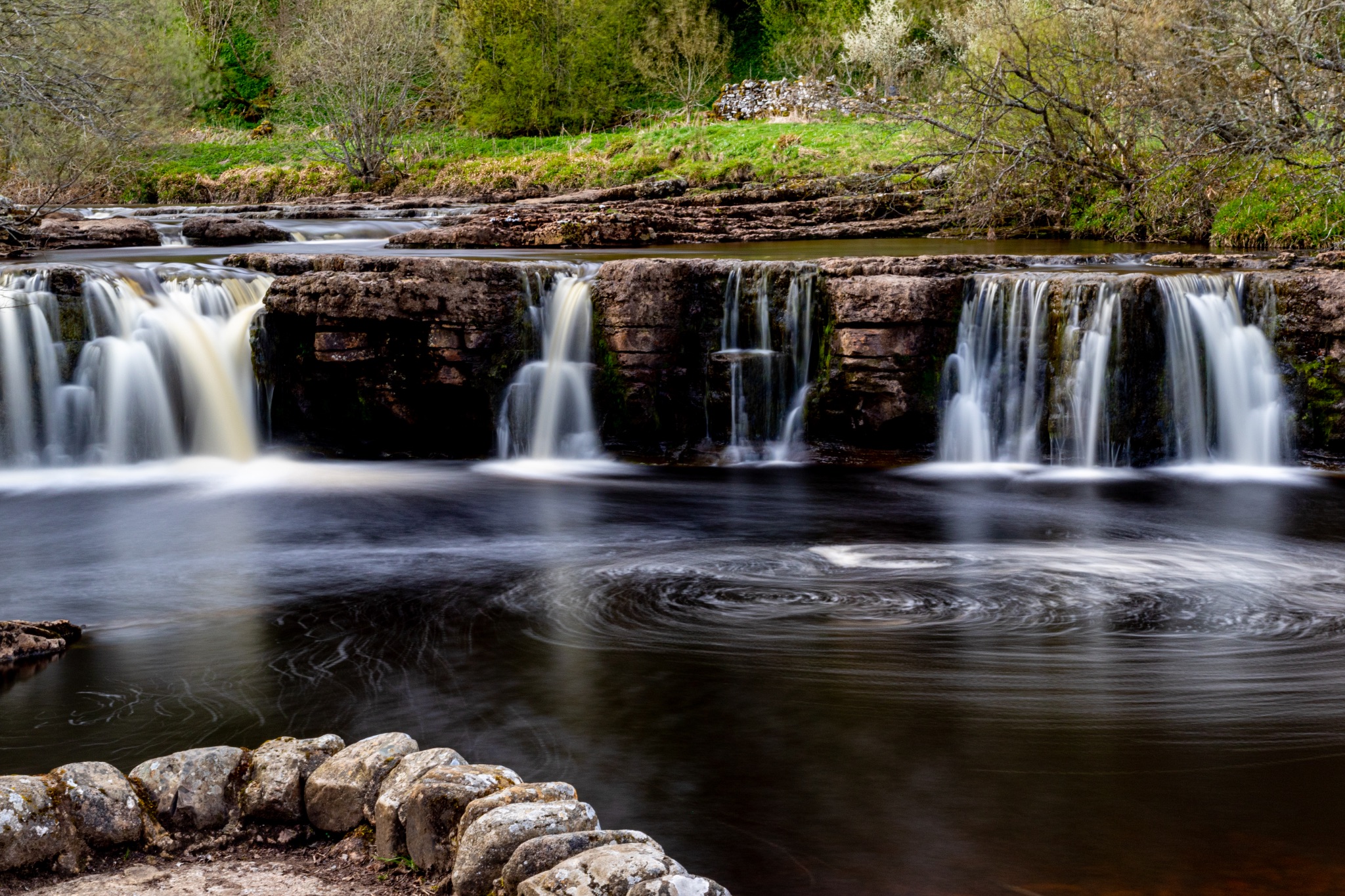 Serene waterfall cascading over rocks in a lush forest, captured with a slow shutter speed for a smooth water effect.