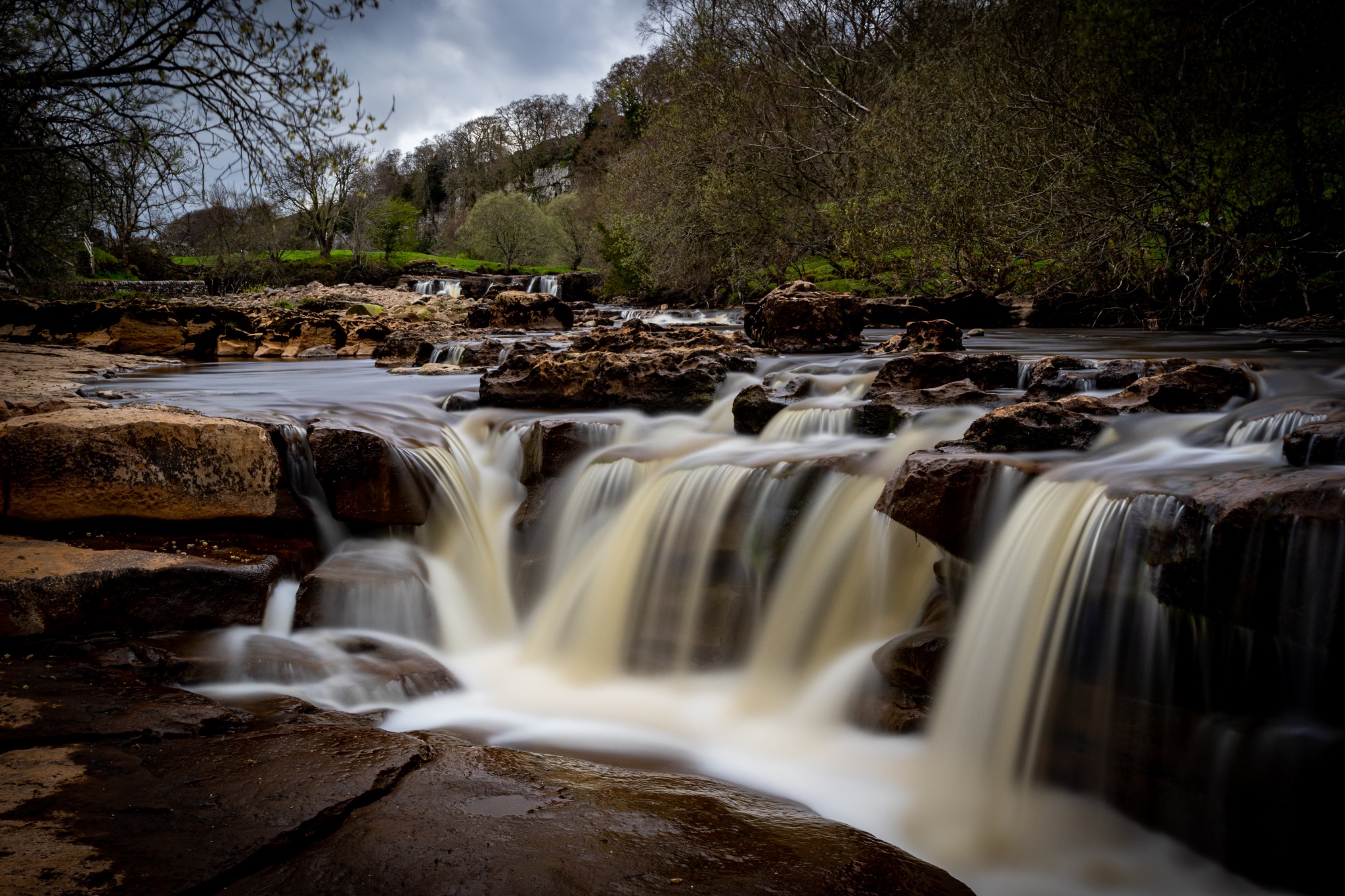 Serene waterfall cascading over rocks with lush greenery in the background, showcasing nature's tranquility.