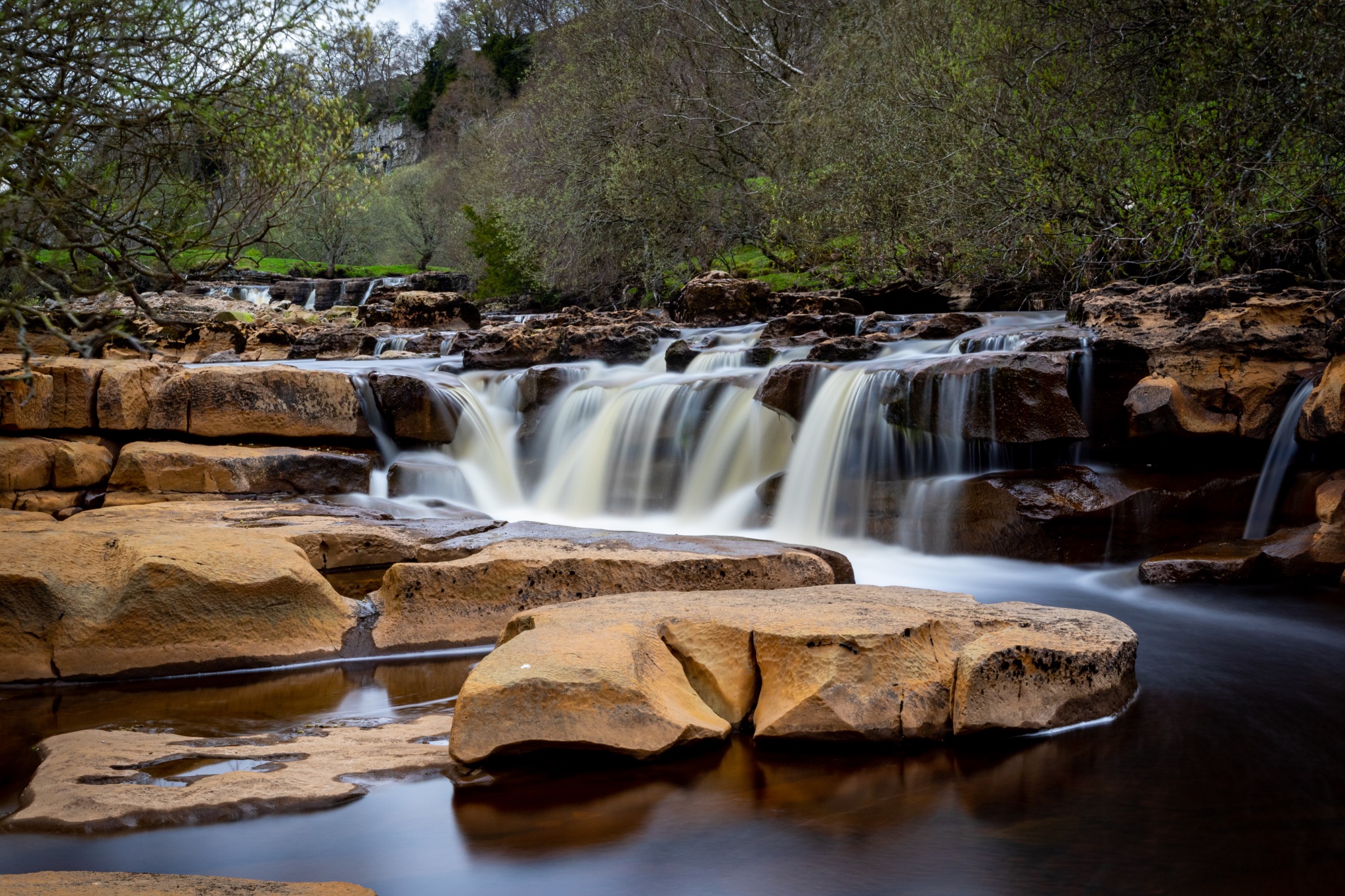 Serene waterfall cascading over rocks with lush greenery in the background, showcasing nature's tranquility.