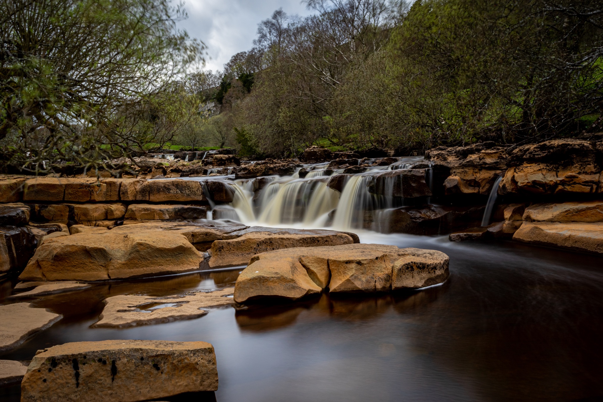 Serene waterfall cascading over rocks with lush greenery in the background, showcasing nature's tranquility.